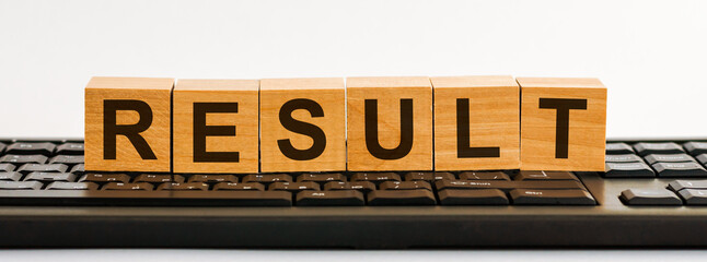 RESULT word made with building blocks. A row of wooden cubes with a word written in black font is located on a black keyboard.