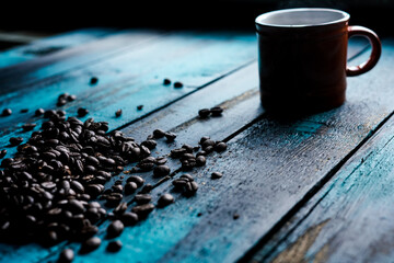 Fototapeta na wymiar morning coffee in an orange cup with roasted whole coffee beans on blue wooden table