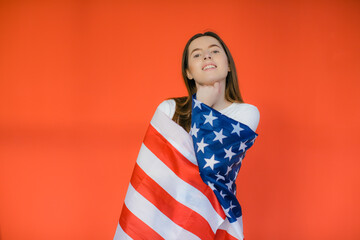 Celebrating an Independence day. Stars and Stripes. Young woman with the flag of the United States of America isolated on red studio background. Looks crazy happy and proud as a patriot of her count