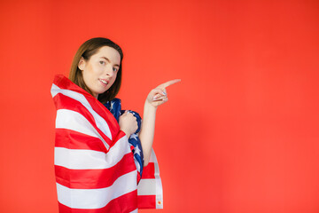 Celebrating an Independence day. Stars and Stripes. Young woman with the flag of the United States of America isolated on red studio background. Looks crazy happy and proud as a patriot of her count