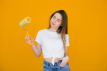 smiling handywoman with hand on hip holding paint roller on yellow background