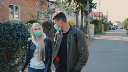 Medium shot of Multiethnic man and woman in medical masks walking down the street in housing estate. They spending their free time together.
