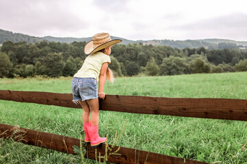 Local vacation, stay safe, stay home. Little girl in cowboy hat playing in western in the farm