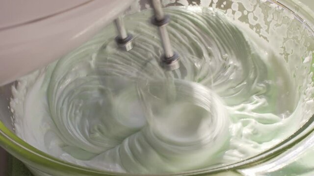 Metal whisks of a hand mixer whipps egg whites with sugar syrup. Cooking italian meringue at home.