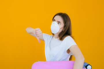 young woman in protective mask with USA flag holding pink suitcase on yellow background. Flight cancellation. Travel industry financial crisis. Quarantine isolation measure