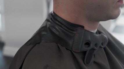 Handsome man is getting trendy haircut in salon. The stylist prepares the client