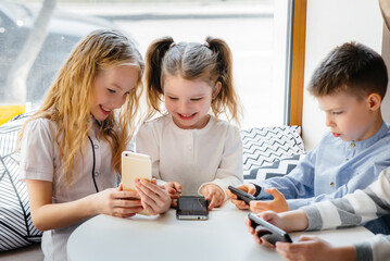 Children sit at a table in a cafe and play mobile phones together. Modern entertainment