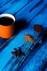 top view roasted and grounded coffee beans in different sizes with orange cup of coffee on blue wooden table
