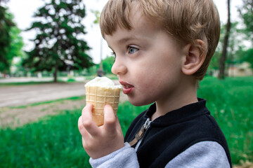 three year old boy eating ice cream in a waffle cup in a park. summer walks with your favorite food. junk food. close-up