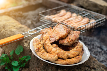 meat and sausages cooked on the grill at the stake. Half is on the plate and some is grilled. summer picnic in nature.