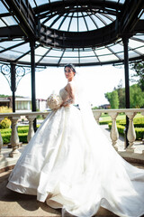 Beautiful young bride with a bouquet. Portrait on the balcony. Wedding makeup and hairstyle. Model. Morning of the bride on the wedding day. She stands on the balcony and looks at the street. Bride.