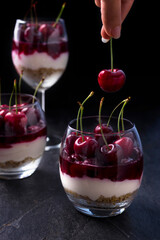 Layerd cherry cheesecake in a glass. Dessert made of bisquits, ricotta, cream, cherry jelly and fresh fruits
