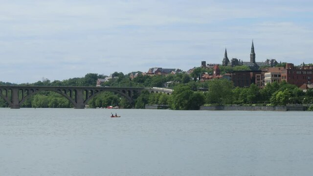 Two people paddle on the Potomac River in a tandem kayak in Washington, D.C.. Key Bridge and the Georgetown Skyline are seen in the background.