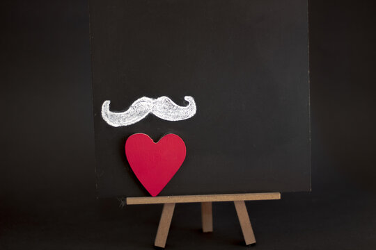 Black chalkboard on black background with white mustache and a heart