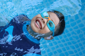 Happy child playing in blue colour swimming pool. Boy with swimming goggles. Kid practice water sport. Summer vacation concept.