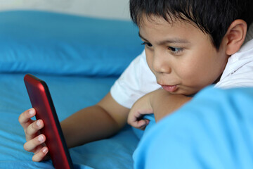 The boy playing games on smartphone. Child using a smartphone while lying on the bed. Social and technology concept.