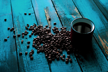 roasted coffee beans on turquoise old wooden table with filtered coffee in orange glass