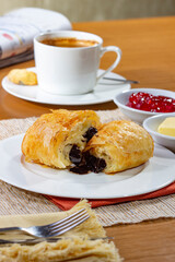 Breakfast with melted chocolate filled Croissants and a cup of coffee, accompanied by a newspaper. Croissants with strawberry jam and butter.