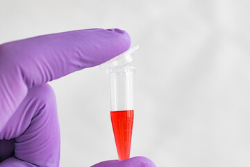 Red sample in a 1.5 ml microcentrifuge tube in gloved hand