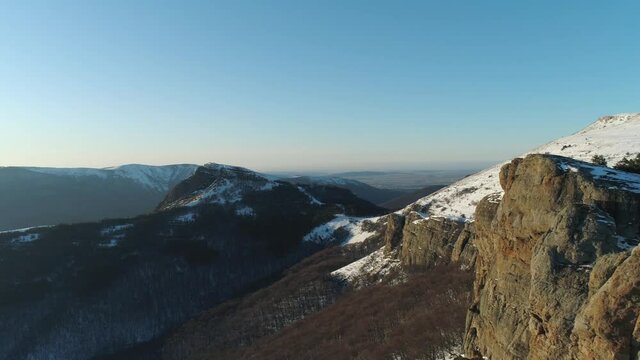 Landscape of snow covered cliffs on a suny day on blue sky background. Shot. Aerial view of sheer cliffs and green dense forest located on their slopes and down in the gorge.