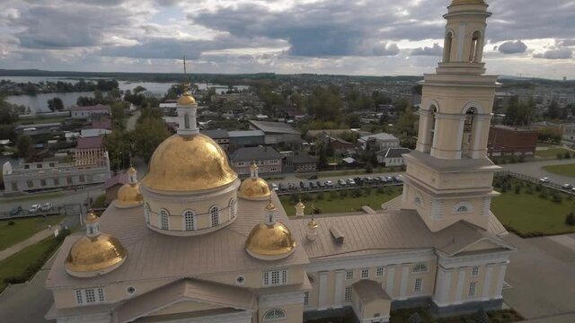 Aerial view of the beautiful white church with a tower and gold domes, religion and faith concept. Stock footage. Flying over the church with city buildings and blue cloudy sky on the background.