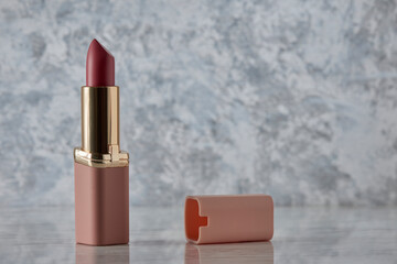Labial rosa con su tapa tirada a un costado sobre una superficie de mármol blanco y espacio para...