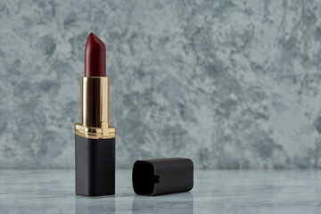 Labial color  vino con negro sobre una superficie de marmol con un fondo de color blanco con gris y...