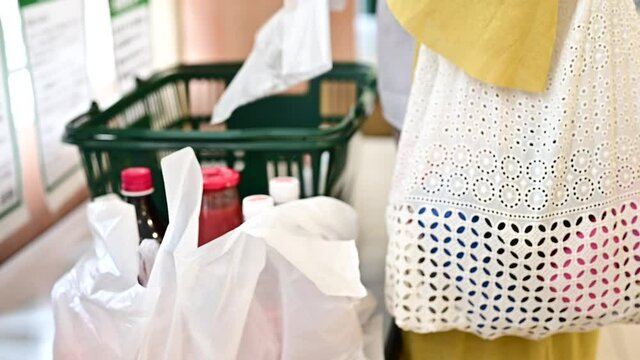 スーパーマーケットで購入した商品をレジ袋に詰める女性