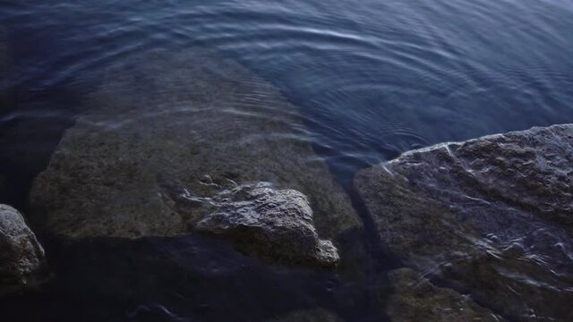 Natural crystal clear fresh shallow water shines and flows on pretty stone lake bottom, static close up