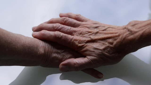 Crystal clear table where an old mom places her hand, then an old dad  puts his hand on, and finally, the young son places his hand over both of them as a sign of family love.