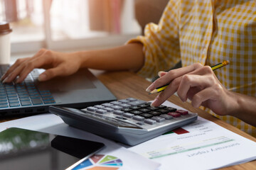 Young businesswoman working on desk with calculator calculate income expense and keying data onto the computer