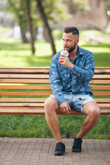 A guy with lemonade is resting in a park on a bench in the spring. Sunny day.