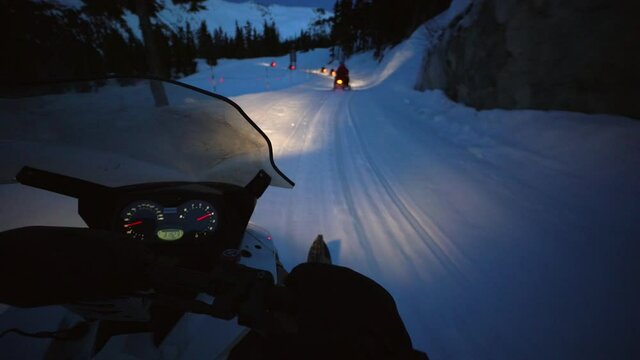 Slow motion shot of snowmobiles on snow by trees and rocks at night - Whistler, British Columbia