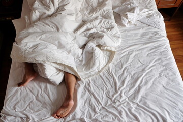Close-up man feet alone in white bed, view of feet man sleeping and lying under white blanket and white bed , couples feet crossed under the duvet in bed