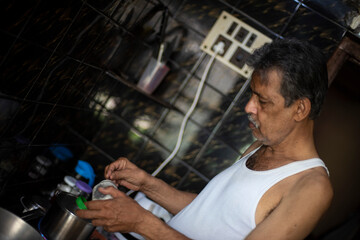 Old/aged Indian Bengali man with beard is making tea in his kitchen wearing casual dress. Indian lifestyle and seniors