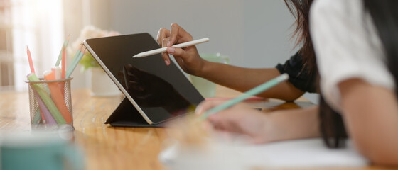 Two college students doing their assignment together with digital tablet and stationery on wooden...