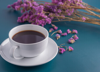 Close-up of a white coffee cup with purple flower blur background. 