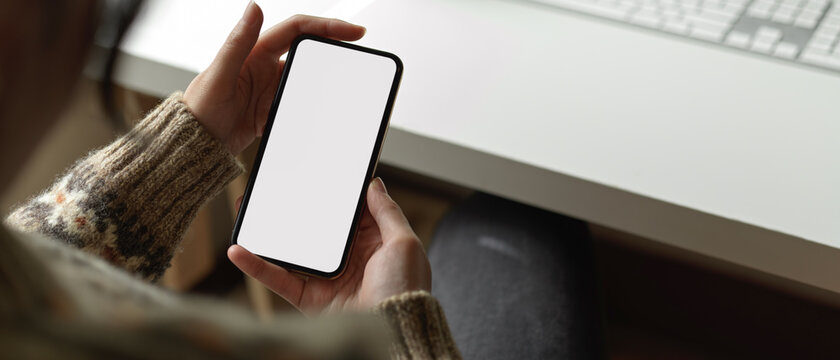 Female employee using mock-up smartphone to contact customer while sitting at office desk
