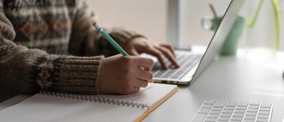 Female university student online learning with laptop and stationery on worktable at home