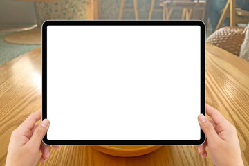 Two hands holding white screen mockup tablet computer in cozy indoor cafe with daylight