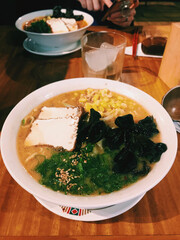 Vegan ramen with corn, tofu, seaweed, green onion, sesame and sauce in a white bowl on a wooden table