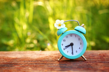 Alarm clock with wild strawberry flowers on a wooden table on a background of grass. The concept of...