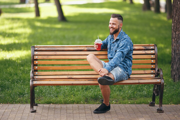 A guy with lemonade is resting in a park on a bench in the spring. Sunny day.