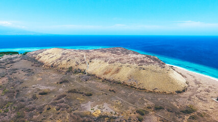 Fototapeta na wymiar Beautiful summer island with dry grass. Paserang Island in West Sumbawa, Indonesia. The yellow land with small hill and blue sky. Aerial image captured by drone.