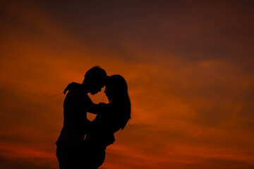 a silhouette of a couple embracing against a bright orange sunset sky.