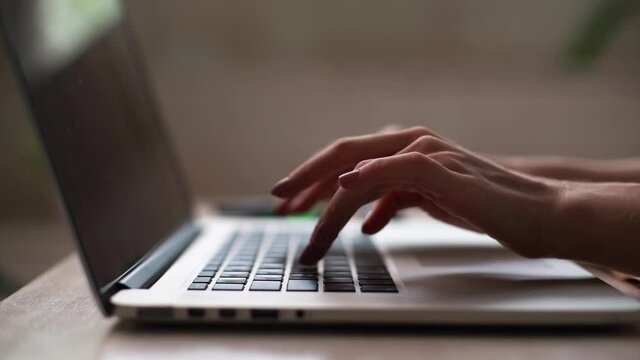 Close-up of hands of unrecognizable woman working on laptop keyboard at remote workplace. Female professional is typing computer. Closeup finger using keyboard in office. Tracking shot in slow motion