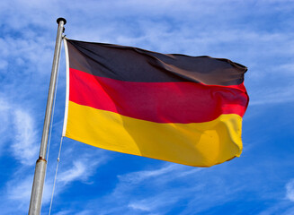 German flag dancing in the wind on a flag pole with the blue sky in the background.