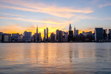 Manhattan Midtown skyline wide angle view on Empire State building, Chrysler building, American Copper Buildings, Headquarters of the United Nations. Sunset, orange sky, reflections in water