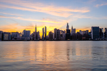 Fototapeta premium Manhattan Midtown skyline wide angle view on Empire State building, Chrysler building, American Copper Buildings, Headquarters of the United Nations. Sunset, orange sky, reflections in water