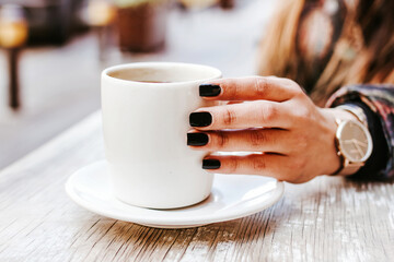 woman hand holding a cup of coffee outdoors at coffee shop or cafe with blurred background